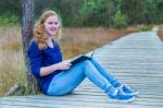 Dutch Girl Reading Book On Wooden Path In Forest Stock Photo