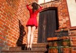 Young Woman In Red Dress Is Standing With Her Back On The Stairs Stock Photo