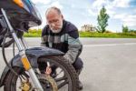 Elderly Man Checks His Motorcycle's Wheel Stock Photo