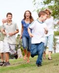 Family Chasing Young Kid In The Park Stock Photo
