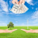 Hand Holding Wind Turbine With Tree And Us Dollars Banknote Stock Photo