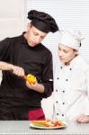 Senior Chef Teaches Young Chef To Decorate Fruit Stock Photo