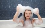 Little Girl Sitting In A Bath And Imposes Soap Suds On Her Head Stock Photo