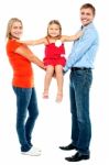 Baby Girl Sitting On Outstretched Arms Of Her Parents Stock Photo