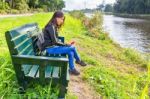 Woman Operating Mobile Phone On Bench At River Stock Photo