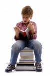 Front View Of Boy Sitting On Books Stock Photo