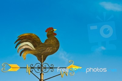 A Cockerel Wind Vane Against Blue Sky Stock Photo