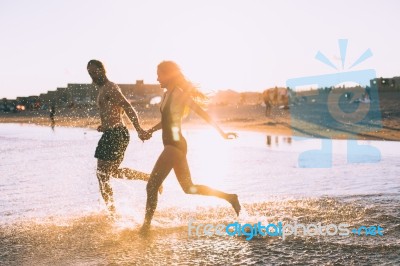 A Couple Is Running On Beach While The Sun Is Set Stock Photo