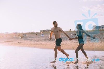 A Couple Is Running On Beach While The Sun Is Set Stock Photo