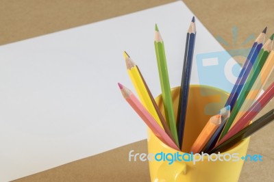 A Lots Of Colour Pencil In Yellow Cup And White Paper On Backgro… Stock Photo