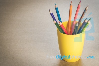A Lots Of Colour Pencils In Yellow Cup On Wooden Texture Paper Stock Photo