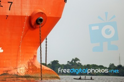 A Small Wooden Canoe Face To Face A Large Orange Ship Near The Port Of Abidjan In Ivory Coast Stock Photo