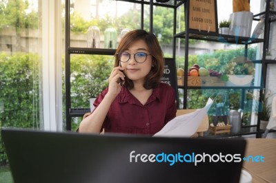 A Young Lady Wears Glasses Working On Laptop And Talking On A Mo… Stock Photo