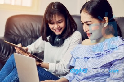 Asian Girl In Blue Casual Dress Listening To Music From Black Headphones And Use Laptop. In A Comfortable And Good Mood, In The Living Room On The Sofa Stock Photo