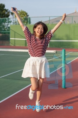 Asian Woman In Sport Tennis Course Jumping With Happiness Emotion Stock Photo