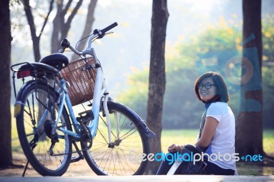 Asian Woman Sitting In The Park With Bicycle In Morning Stock Photo