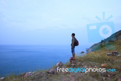 Backpack Man Standing On Rock Mountain And Looking To Ocean Use Stock Photo