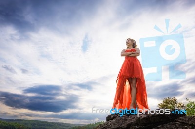 Beautiful Woman Wear Red Evening Dress Stand On The Rocks Over M… Stock Photo
