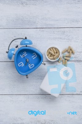 Blue Clock With Herb Capsule On Wood Background Stock Photo