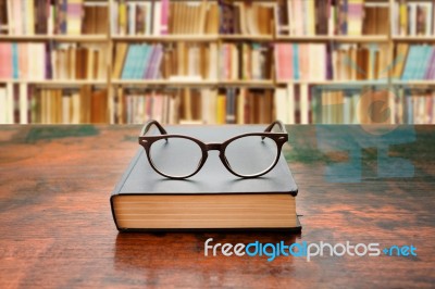 Book With Glasses On The Desk Against Library Stock Photo
