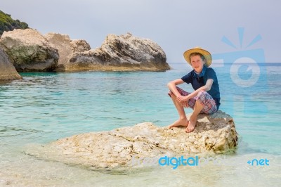 Boy With Hat Sitting On Rock In Sea Stock Photo