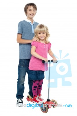 Brother Holding Her Sister As She Rides Her Toy Scooter Stock Photo