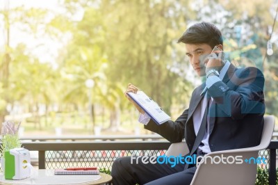 Business Man Using Mobile Phone And Hold A Report Paper  While S… Stock Photo
