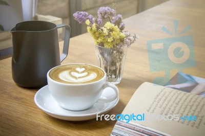Cappuccino Coffee Cup With Decorative Flowers And Opened Book On Table Stock Photo