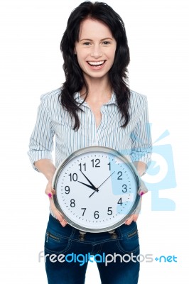 Cheerful Brunette In Casual Presenting A Wall Clock Stock Photo