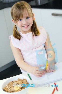 Child Drawing With Crayons, Sitting At Table In Kitchen At Home Stock Photo