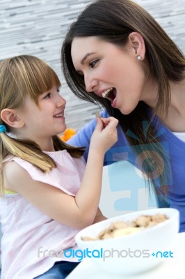 Child Eating Cereals With Her Mom In The Kitchen Stock Photo