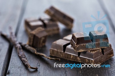 Chunks Of Dark Chocolate Bar And Vanilla Beans On Wooden Table Stock Photo