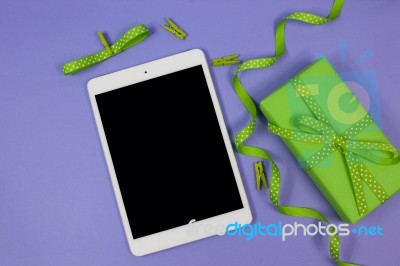 Digital Tablet With Green Gift With Polka Dot Ribbon On Lilac Background Stock Photo