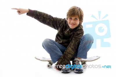 Front View Of Boy Sitting On Skate And Pointing Stock Photo