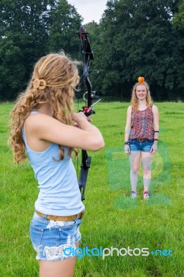 Girl Aiming Arrow Of Compound Bow At Apple On Head Of Woman Stock Photo
