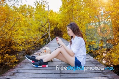 Girl Sitting Alone And Hand Holding Camera On A The Wooden Bridge In Autumn Stock Photo