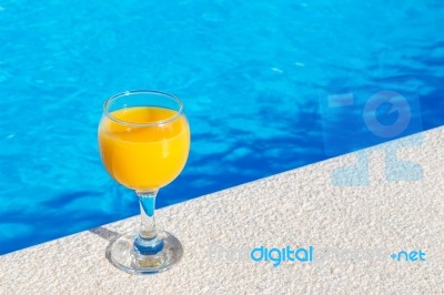 Glass With Orange Juice On Edge Of Swimming Pool Stock Photo