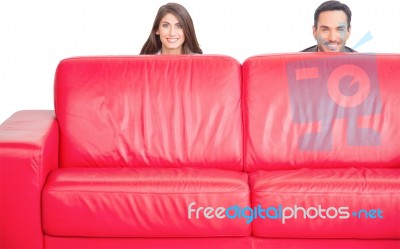 Happy Young Couple Hiding Behind Red Sofa Stock Photo