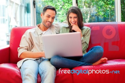 Happy Young Couple Using Laptop On Red Sofa Stock Photo