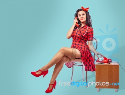 Happy Young Pinup Woman Sitting On A Chair And Talking On Phone Stock Photo
