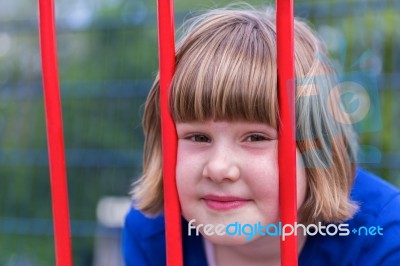 Head Of Young Girl Behind Red Bars Stock Photo