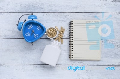 Herb Capsule With Notebook And Blue Clock Stock Photo