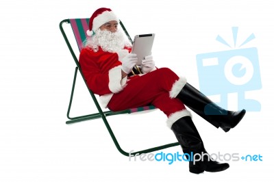 Kris Kringle Relaxing And Using Electronic Tablet Stock Photo