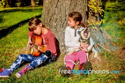 Little Girl Playing Guitare In The Park With Husky Puppy Singing… Stock Photo