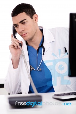Male Doctor Sitting At The Desk Talking Over Phone Stock Photo