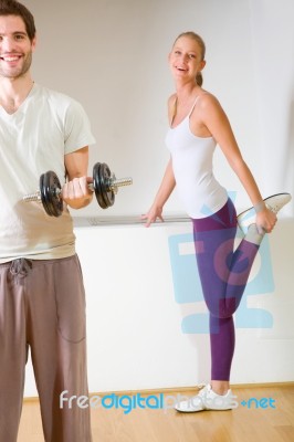 Man Lifting Dumbbell And Woman Stretching In Gym Stock Photo