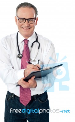 Matured Doctor Writing On Clipboard Stock Photo