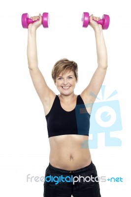 Mid Adult Woman Holding Dumbbells Over Head Stock Photo