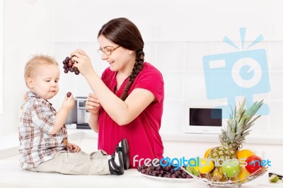 Mother Feeding Child In Kitchen Stock Photo
