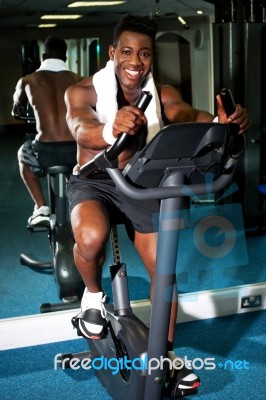 Muscular Man On Excercise Bike At The Gym Stock Photo